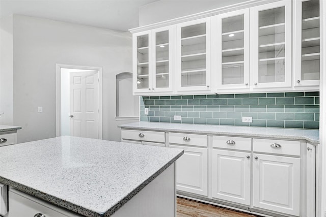 kitchen featuring glass insert cabinets, white cabinetry, light stone countertops, and tasteful backsplash