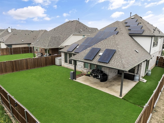 rear view of property featuring a fenced backyard, roof with shingles, a patio area, a yard, and solar panels