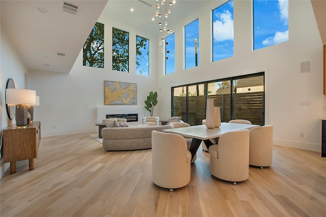 dining room featuring visible vents, baseboards, a glass covered fireplace, light wood-style floors, and a high ceiling