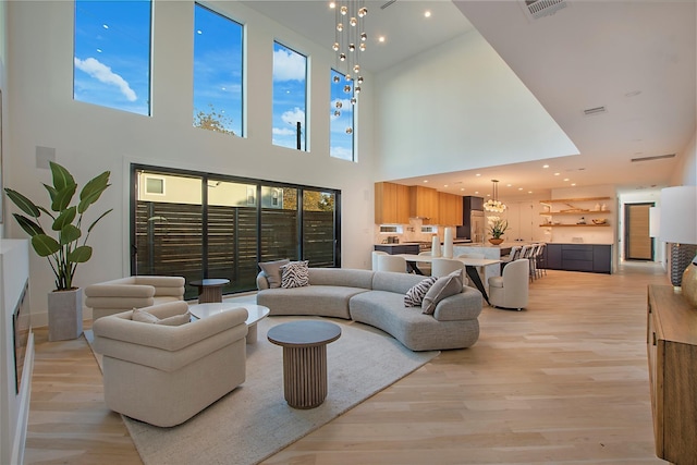 living room with visible vents, light wood-style floors, a high ceiling, and an inviting chandelier