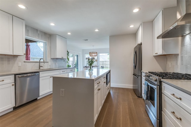 kitchen with a sink, stainless steel appliances, wall chimney exhaust hood, and wood finished floors