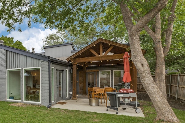 rear view of property with a lawn, brick siding, fence, and a patio