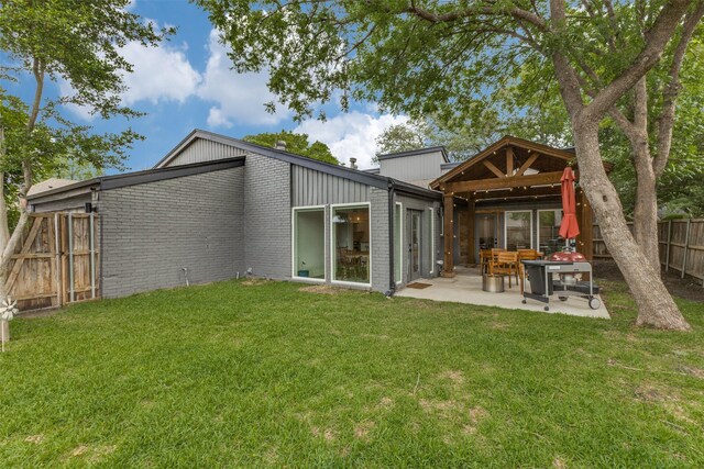 rear view of property with a lawn, a patio area, brick siding, a gazebo, and a fenced backyard
