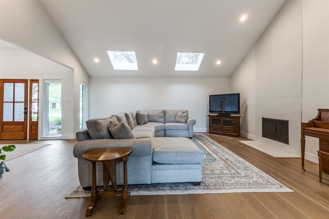 living area with wood finished floors, high vaulted ceiling, recessed lighting, a large fireplace, and a skylight