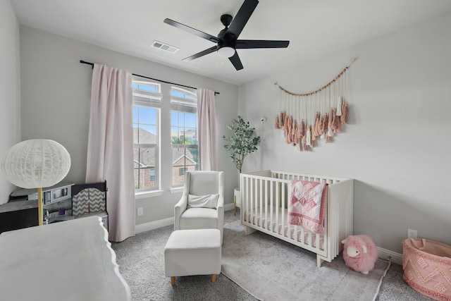 carpeted bedroom featuring a crib, visible vents, baseboards, and ceiling fan