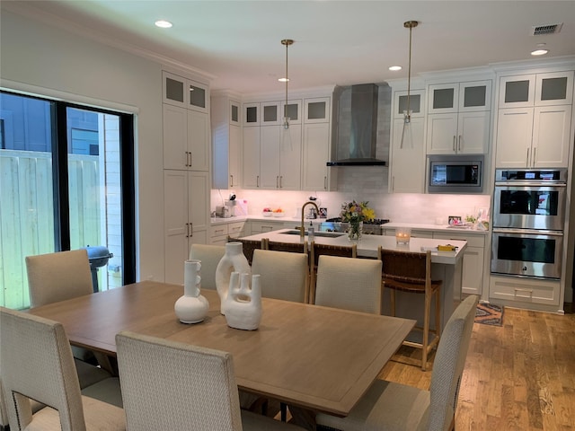 kitchen with visible vents, a center island with sink, wall chimney exhaust hood, a sink, and stainless steel appliances