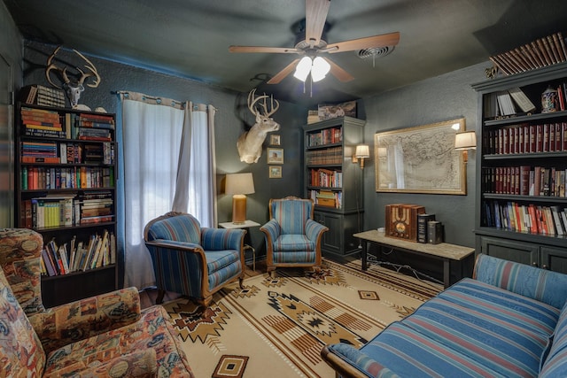sitting room with a textured wall and ceiling fan