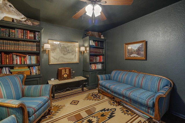 sitting room featuring a ceiling fan, a textured wall, and vaulted ceiling