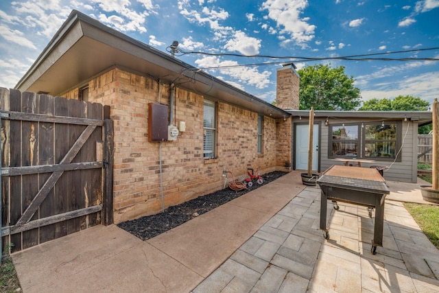 view of side of home with fence, a patio, a chimney, brick siding, and a gate