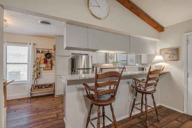 kitchen with decorative backsplash, freestanding refrigerator, a kitchen breakfast bar, and dark wood-type flooring