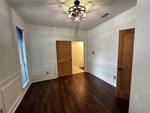 spare room featuring wood finished floors, a wainscoted wall, a textured ceiling, visible vents, and a decorative wall