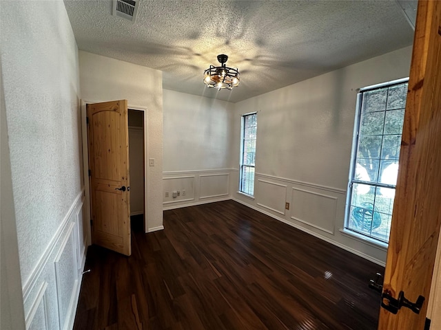 unfurnished bedroom with a decorative wall, visible vents, a textured ceiling, and dark wood-type flooring