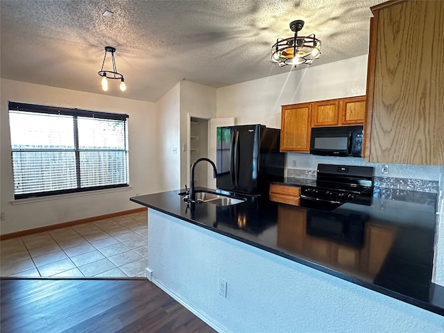 kitchen with a textured ceiling, a sink, brown cabinets, black appliances, and dark countertops