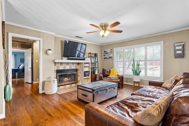 living room featuring crown molding, a ceiling fan, wood finished floors, and a tile fireplace