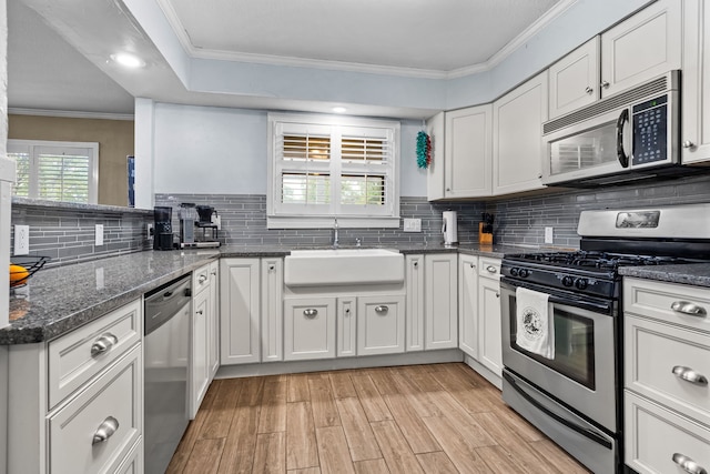 kitchen with a sink, white cabinets, light wood-style floors, ornamental molding, and stainless steel appliances