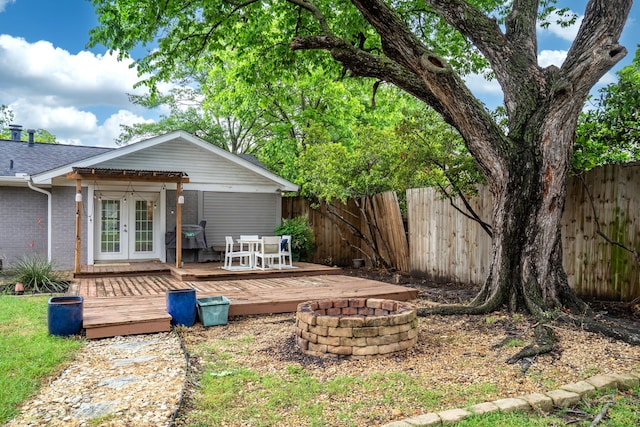 rear view of house with a fire pit, a wooden deck, french doors, and fence
