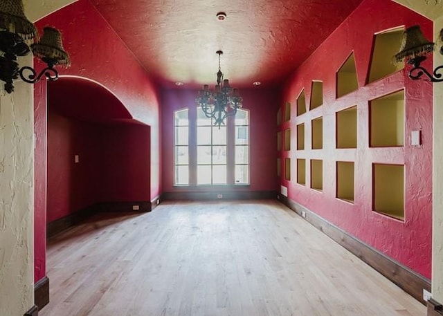 unfurnished dining area featuring a textured wall, a chandelier, and wood finished floors