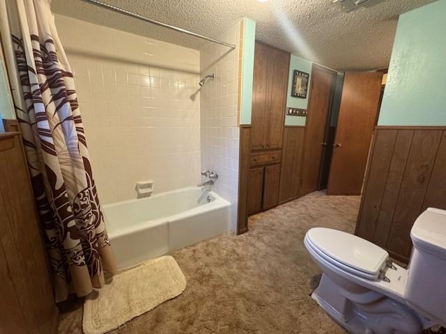 bathroom with a textured ceiling, shower / bath combo, a wainscoted wall, toilet, and wooden walls
