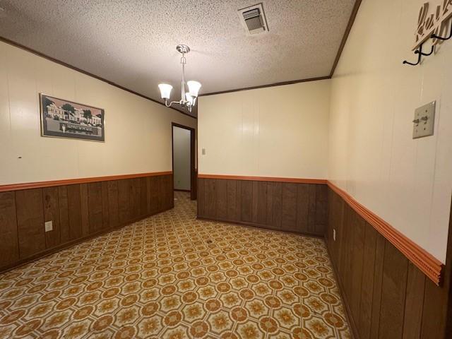 spare room with wooden walls, a notable chandelier, visible vents, and wainscoting