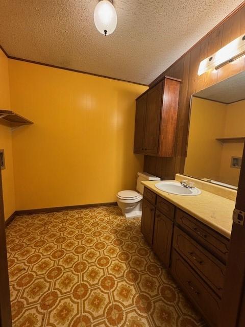 bathroom with toilet, a textured ceiling, baseboards, and vanity