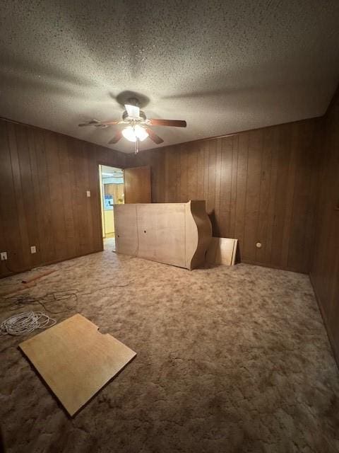 unfurnished bedroom featuring wooden walls, a ceiling fan, a textured ceiling, and carpet floors