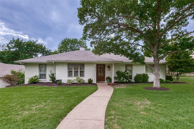single story home featuring roof with shingles, a chimney, brick siding, and a front yard