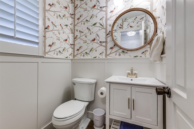 half bath featuring vanity, a wainscoted wall, a decorative wall, and wallpapered walls