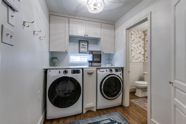 laundry area with an inviting chandelier, washing machine and dryer, cabinet space, and wood finished floors