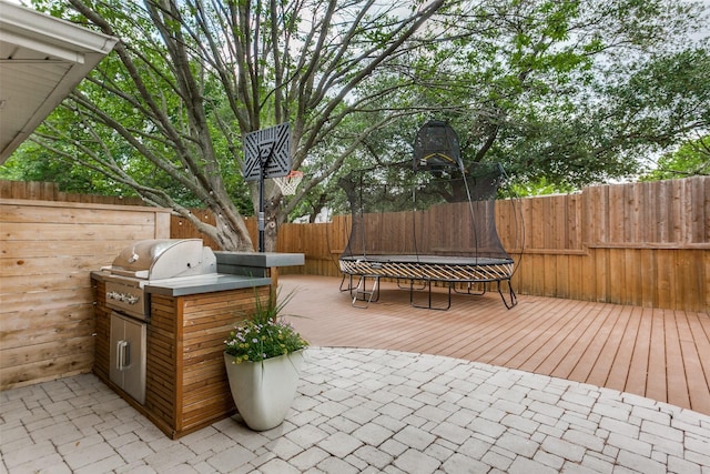 view of patio / terrace with area for grilling, a deck, a fenced backyard, and a trampoline