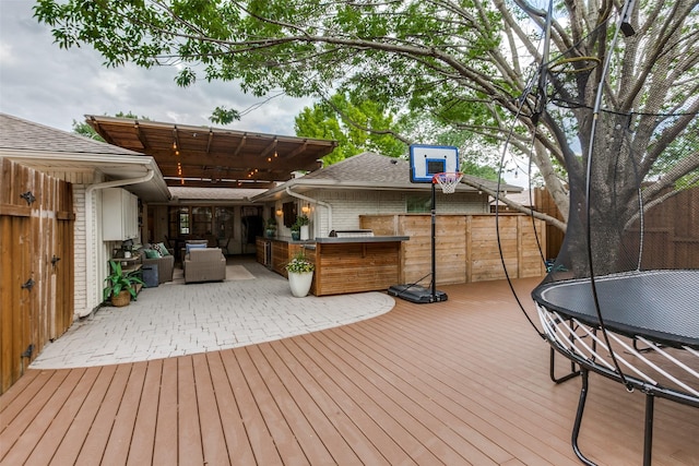 wooden terrace with outdoor lounge area, a trampoline, and outdoor dry bar