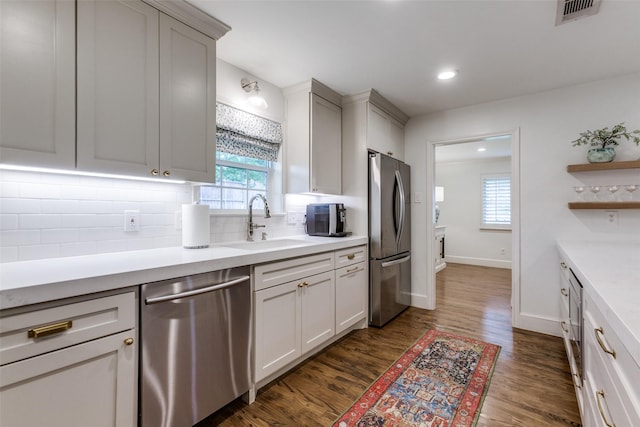 kitchen featuring visible vents, dark wood-style floors, a sink, backsplash, and stainless steel appliances