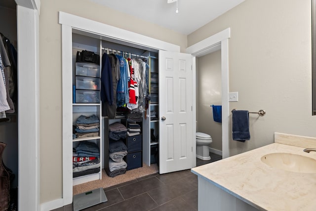 bathroom featuring tile patterned flooring, a spacious closet, toilet, and vanity