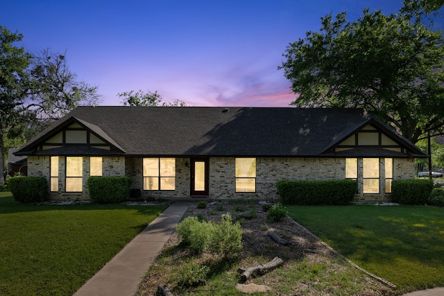 english style home with a yard, brick siding, and a shingled roof