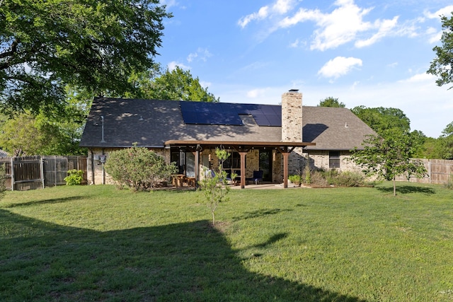 back of house with roof mounted solar panels, a patio area, and a yard