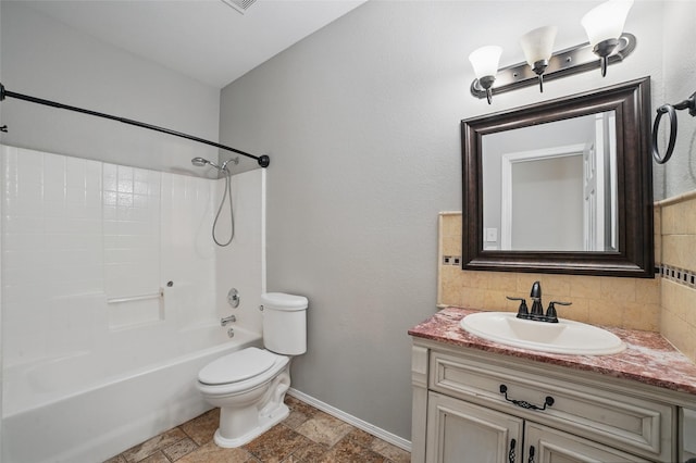 bathroom with backsplash, vanity, baseboards, toilet, and stone tile flooring