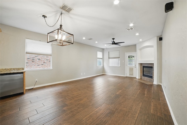 unfurnished living room with visible vents, dark wood-style flooring, ceiling fan with notable chandelier, and a tile fireplace