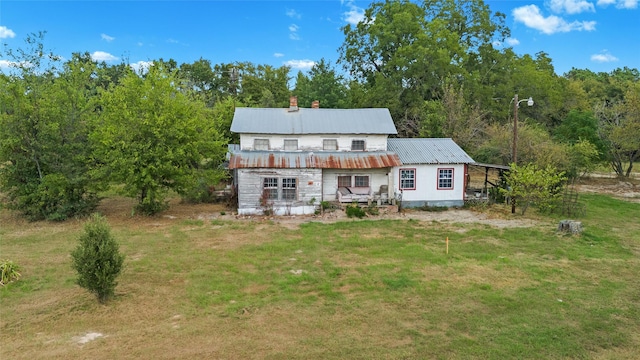 back of house with a lawn, a forest view, and metal roof