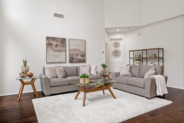 living area featuring baseboards, visible vents, dark wood-type flooring, and a towering ceiling