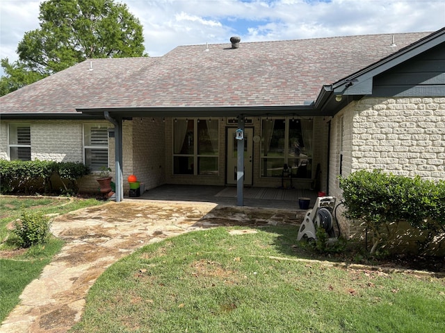 rear view of property featuring a yard, a shingled roof, brick siding, and a porch