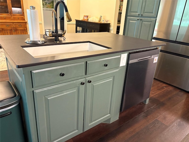 kitchen with green cabinets, a sink, stainless steel appliances, a kitchen island with sink, and dark wood-style floors
