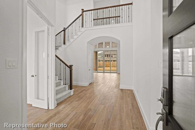 foyer entrance with a towering ceiling, wood finished floors, baseboards, stairway, and arched walkways