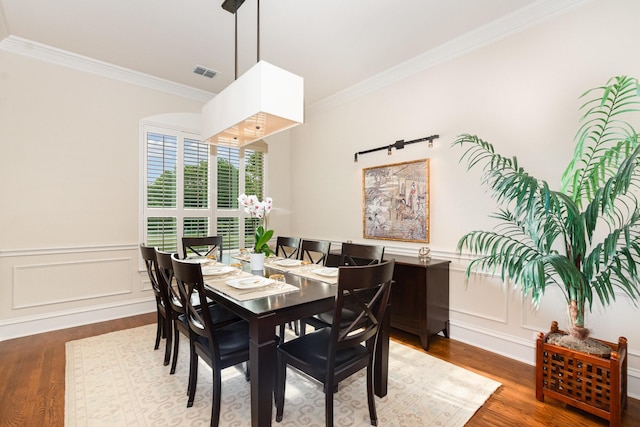 dining area with visible vents, ornamental molding, wood finished floors, and a decorative wall