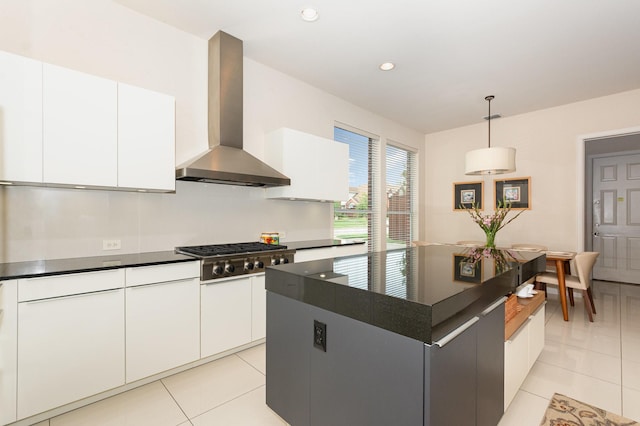 kitchen with wall chimney range hood, light tile patterned flooring, dark countertops, stainless steel gas cooktop, and white cabinetry