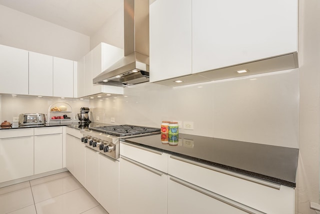 kitchen with white cabinets, dark countertops, stainless steel gas stovetop, and wall chimney exhaust hood