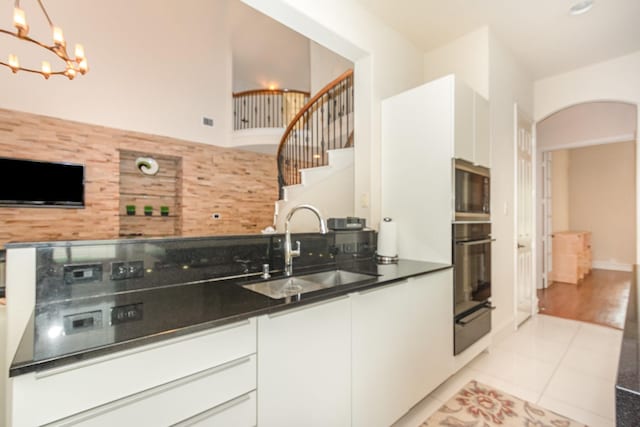 kitchen featuring dark countertops, a sink, black oven, white cabinetry, and a warming drawer