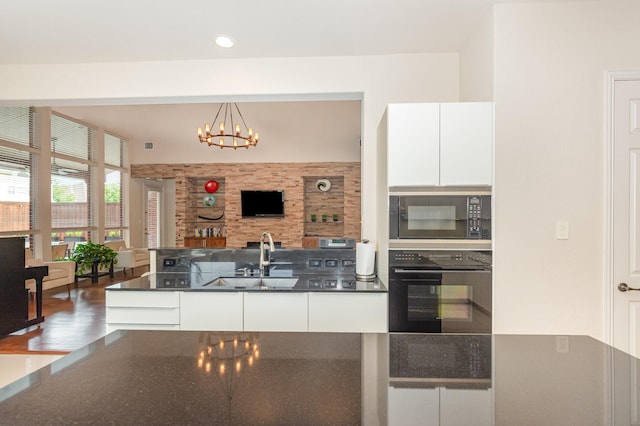 kitchen featuring modern cabinets, white cabinetry, a chandelier, a sink, and black appliances