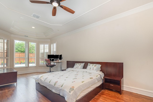 bedroom with ceiling fan, crown molding, wood finished floors, a raised ceiling, and baseboards