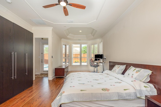 bedroom with crown molding, a tray ceiling, wood finished floors, and visible vents