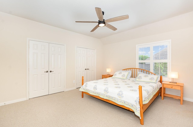bedroom with baseboards, ceiling fan, two closets, and light colored carpet