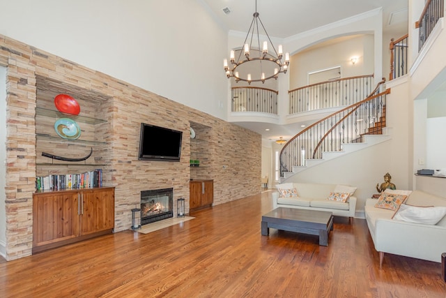 living room with crown molding, stairs, a towering ceiling, wood finished floors, and a fireplace with flush hearth